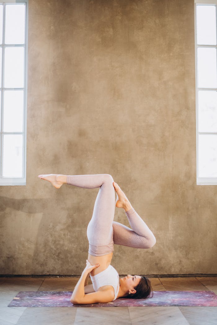 Services A woman performing a yoga shoulderstand pose indoors, focusing on flexibility and relaxation.